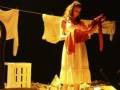 Una mujer en una escena teatral, con ropa colgada en un tendedero.
