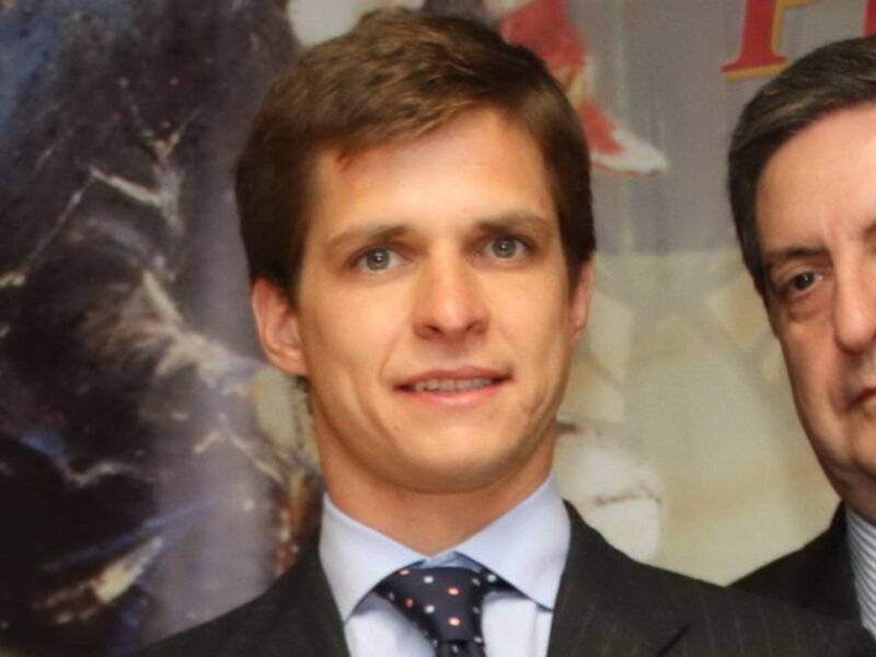 Dos hombres en trajes, uno joven y uno mayor, posando juntos en un evento formal.