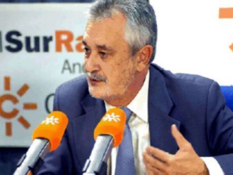 Hombre en traje hablando en rueda de prensa, con micros y logo de 'SurRadio' en el fondo.