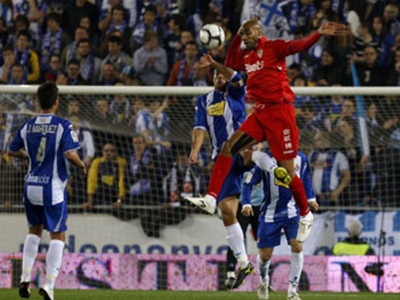 Jugador en rojo realiza un cabezazo durante un partido de fútbol en un estadio lleno de espectadores.