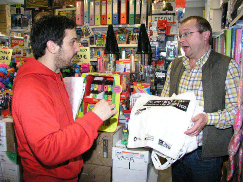 Dos hombres en una tienda de artículos escolares y oficina, intercambiando un producto y una bolsa de regalo.