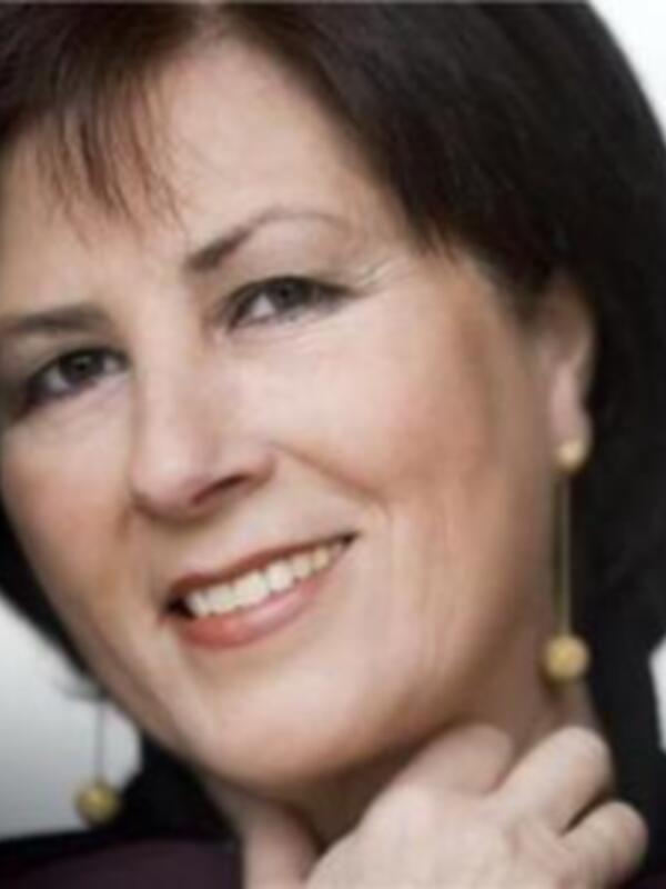 A una persona con cabello corto y negro, llevando un maquillaje suave. La persona está sonriendo y parece estar en una situación formal o profesional, posiblemente en un evento o entrevista.