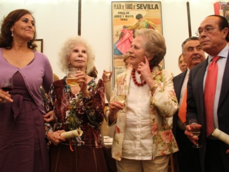 Una celebración formal con cuatro personas, dos de ellas con copas de vino, frente a una pintura de toros en Sevilla.