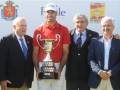 Un golfista sostiene un trofeo junto a cuatro hombres en trajes formales, posando frente a una bandera de España y un cartel de la Ryder Cup.