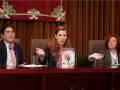 Tres personas sentadas en una mesa, con un libro titulado "La Traviata" entre ellas. El entorno parece ser formal, posiblemente una conferencia o presentación.