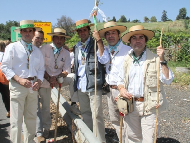 Un grupo de hombres vestidos con trajes tradicionales posa en una carretera, con un cartel de precaución y árboles al fondo.