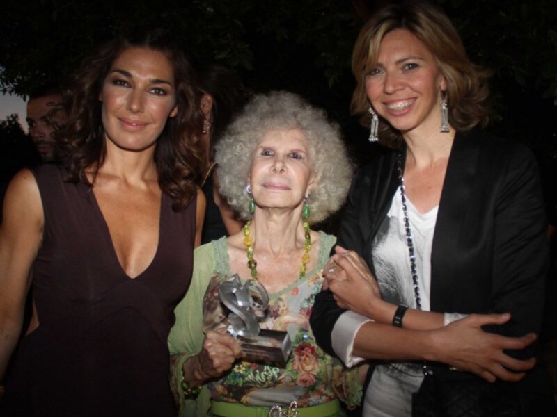 Tres mujeres celebran un momento especial, una de ellas sostiene un trofeo.