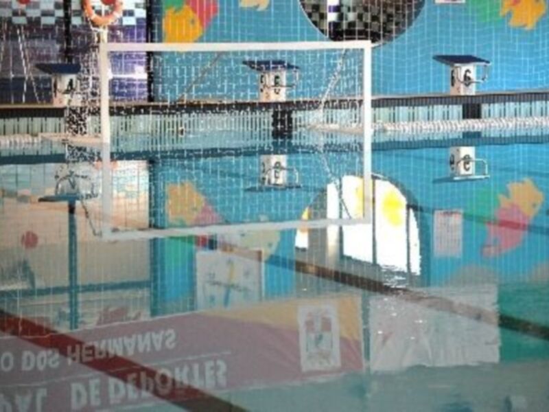 Piscina interior con malla de seguridad y decoración colorida en la pared.