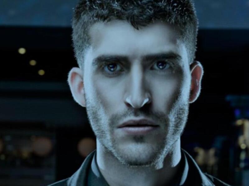 Un hombre con cabello corto y rizado, mirando directamente a la cámara. La imagen está en tonos de azul y negro, con un fondo borroso que parece ser una sala o estudio.