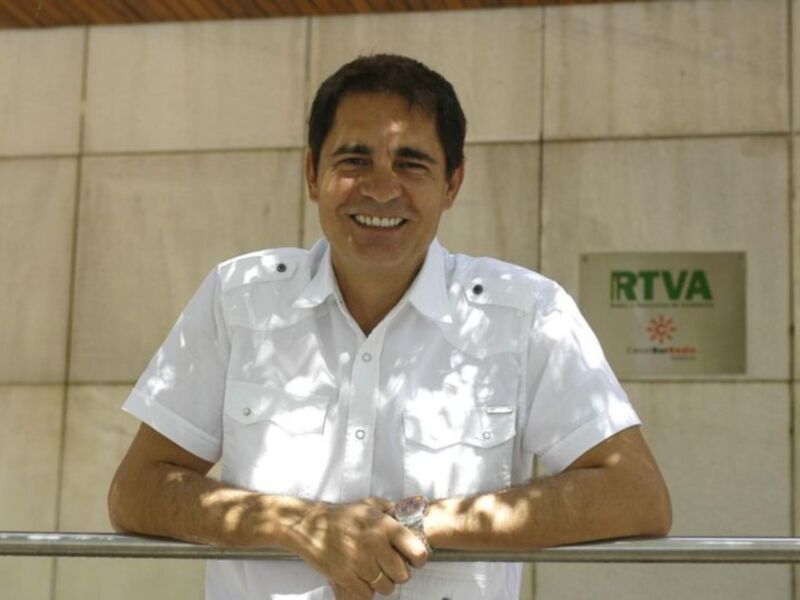 Un hombre sonríe ampliamente mientras sostiene una barra metálica. Detrás de él, se puede ver un muro con una placa que dice "RTVA".