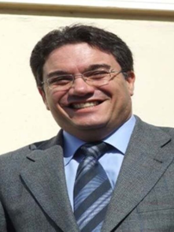 Hombre sonriente en traje y corbata, frente a un fondo neutro.