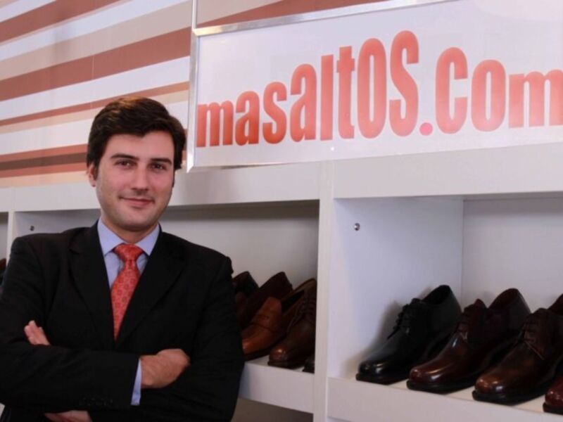 Hombre en traje y corbata frente a estantes de zapatos en una tienda de calzado.