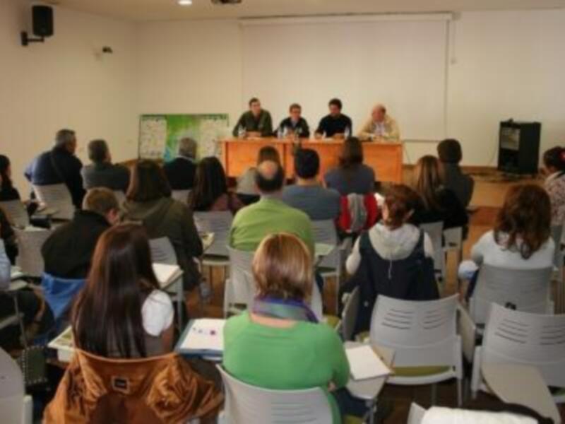 Grupo de personas en una sala de conferencias, escuchando a los ponentes durante una sesión de capacitación.