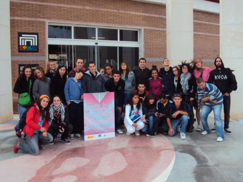 Grupo de estudiantes frente a una fachada de edificio, con una pancarta que indica un evento de juventud.