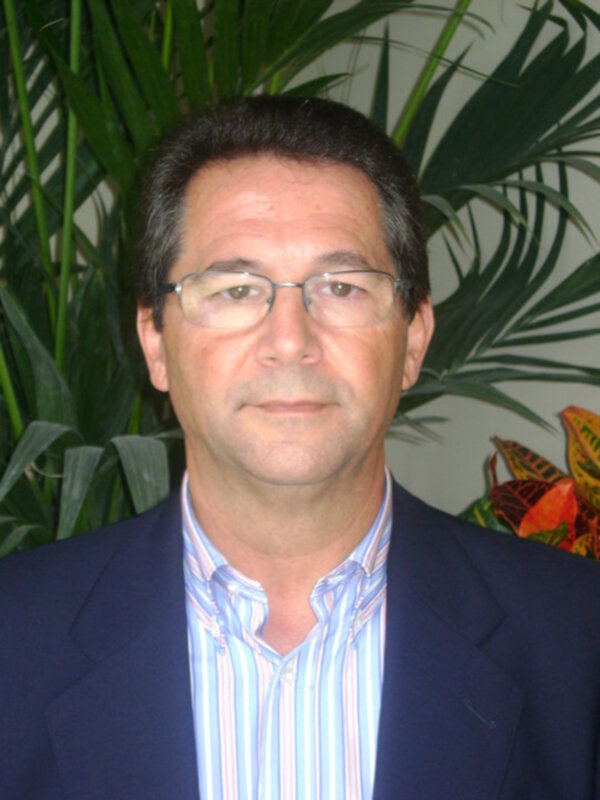 Elegante hombre con gafas y traje azul, posando frente a plantas verdes.