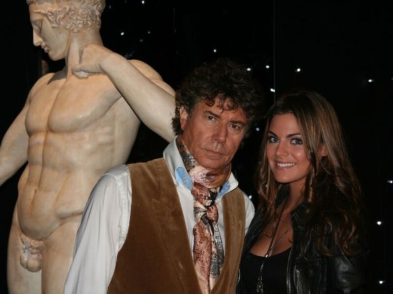 Un hombre y una mujer posan junto a una estatua de un atleta en una exposición cultural.