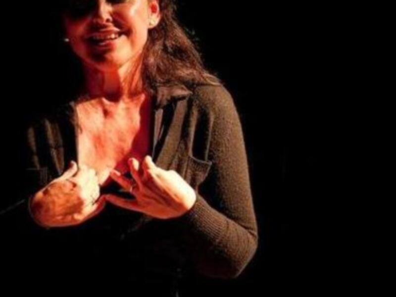Actriz en escena con gestos expresivos, iluminada por foco dramático.