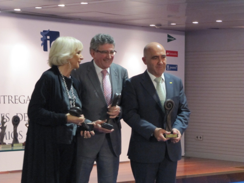 Premiación en una ceremonia formal con tres personas sosteniendo trofeos.