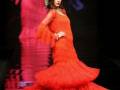 Una mujer vestida con un vestido de flamenco rojo largo y volante, posando en una pasarela.