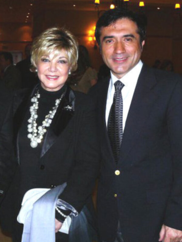 Dos personas sonrientes en trajes formales, posando juntos en un evento formal.