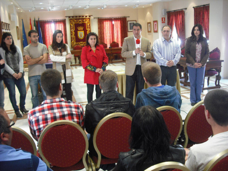 Una reunión en un salón con personas de pie y sentadas, algunos con banderas en el fondo.