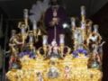 Elegante procesión religiosa con una figura central vestida de morado, rodeada de adornos dorados y flores, en un entorno festivo.