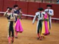 Tres toreros caminan con sus capotes y mantones coloridos en una plaza de toros.