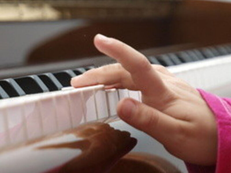 Mano tocando un teclado portátil, con una chaqueta rosa y una guitarra detrás.