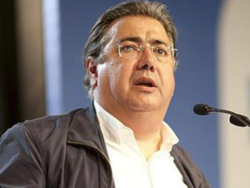 El hombre está hablando en un evento formal, con una camisa blanca y una chaqueta negra. La imagen es clara y detallada, capturando el momento de la charla.