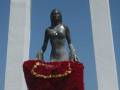 La estatua de una mujer con un vestido rojo y flores en la base, bajo un cielo azul claro.