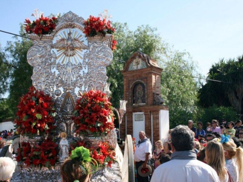 Procesión religiosa con estandarte ornado y devotos en un entorno festivo.