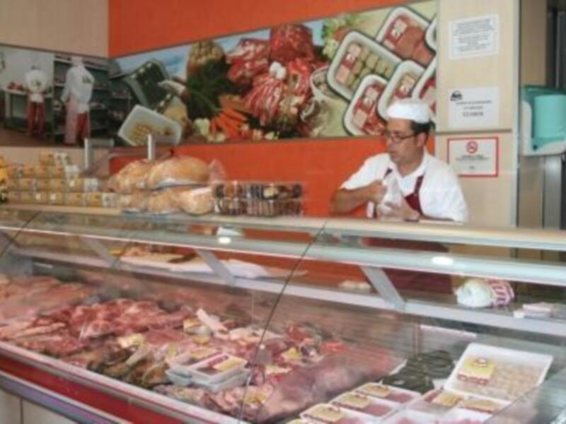 Vendedor en una carnicería, mostrando variedad de carnes frescas y embutidos en un escaparate.