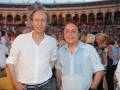 Dos hombres posan frente a una plaza de toros llena de espectadores.
