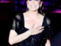 Elegant woman in a glittering black dress, holding her hand to her chest in a gesture of gratitude or emotion.