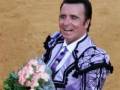 Un torero sonríe satisfecho mientras sostiene un ramo de flores, celebrando una victoria en la plaza de toros.
