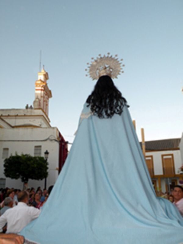 Procesión de la Virgen con manto azul en una plaza histórica.