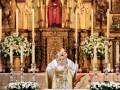 Celebración religiosa en un altar adornado con flores y candelabros, presidido por un sacerdote en traje ceremonial.