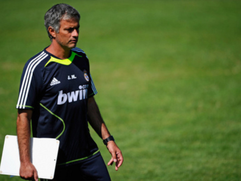 Entrenador caminando en el campo de fútbol, sosteniendo una pizarra.