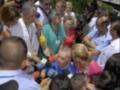 Una persona en un traje médico es entrevistada por una multitud de periodistas con micrófonos y cámaras. La escena parece ser en un evento público o conferencia de prensa.