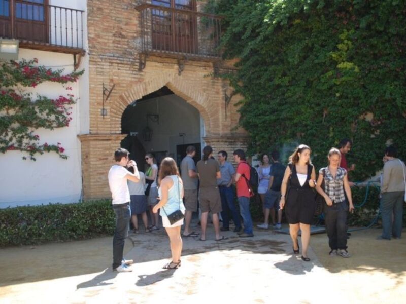 Gente visitando un patio histórico con arcos y flores en la pared.