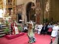 Interior de una iglesia con un altar decorado con flores y velas, personas vestidas con vestidos blancos y rojos, y un altar con imágenes religiosas.