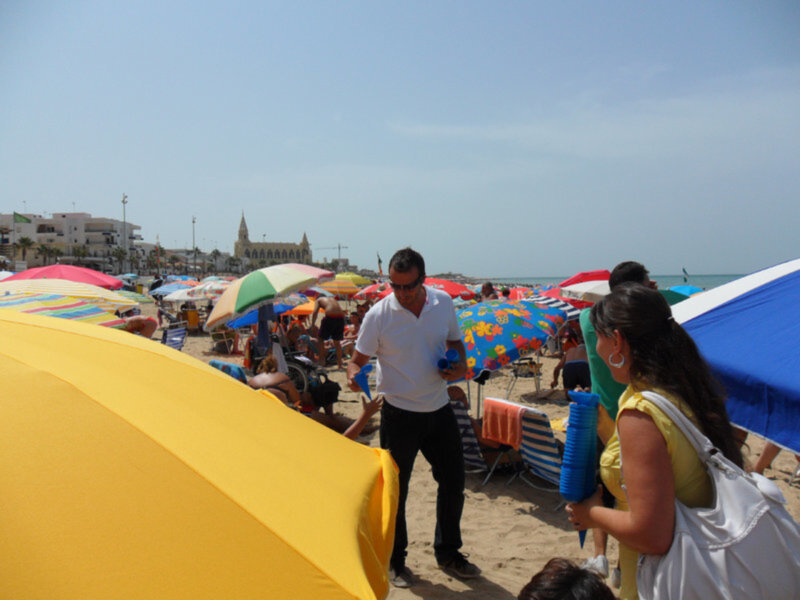 Playa con muchos sombrillas de colores, gente disfrutando del sol y la playa.