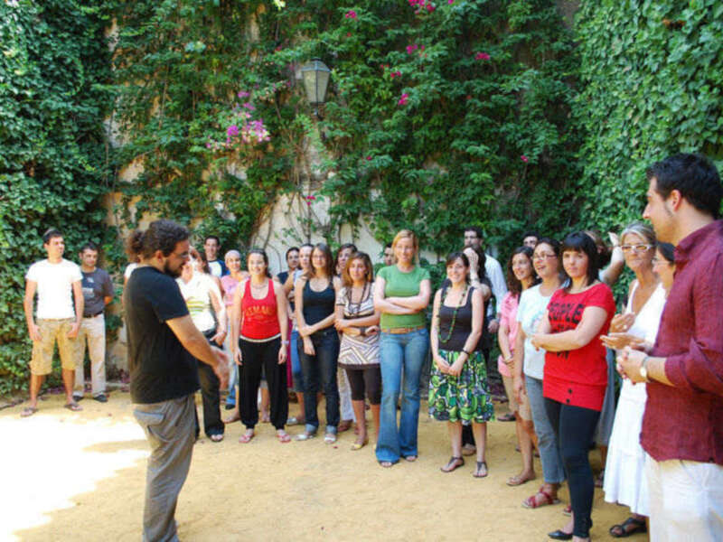 Un grupo de personas participa en una charla o taller al aire libre en un patio con paredes cubiertas de vegetación.