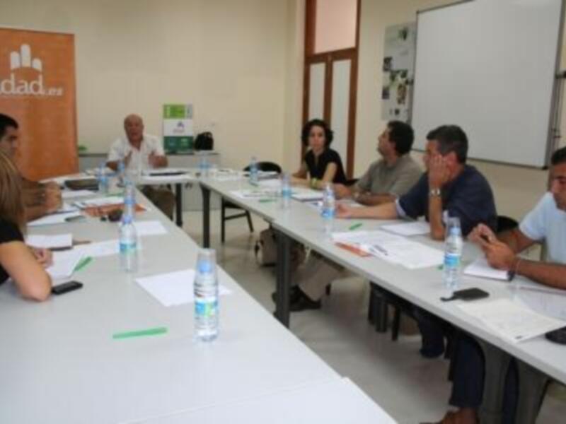 Una reunión de trabajo en un ambiente de oficina con personas sentadas en mesas, utilizando teléfonos y documentos.