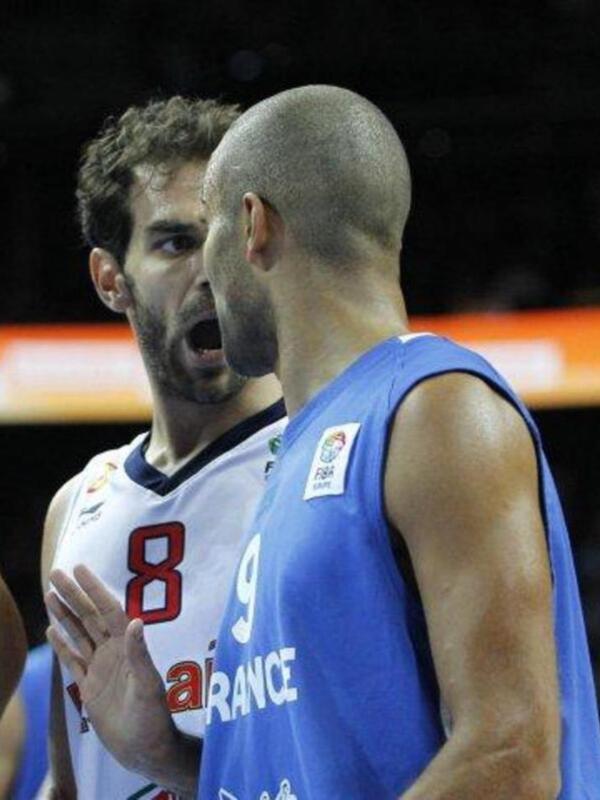 Two basketball players from different teams, one wearing a white jersey with the number 8 and the other in a blue jersey with the number 9, are engaged in a conversation during a game.