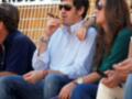 Un hombre fuma un cigarrillo mientras una mujer y otra persona observan la escena. En el fondo, se puede ver un cartel con texto que parece ser "TENDIDO 2".