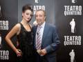 Una mujer con vestido negro y un hombre en traje posan frente a un fondo negro con el logo del Teatro Quintero.