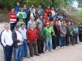 Grupo de personas posando para una foto en un entorno natural con árboles y una colina en el fondo. Algunos individuos están sosteniendo copas de champán, lo que sugiere que podría ser una celebración o evento social.