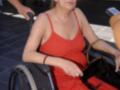 Una mujer en silla de ruedas con vestido rojo, mirando hacia la cámara.