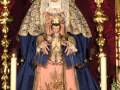 Imagen de una Virgen María vestida con una saya y tocado en un altar decorado con flores y adornos dorados.